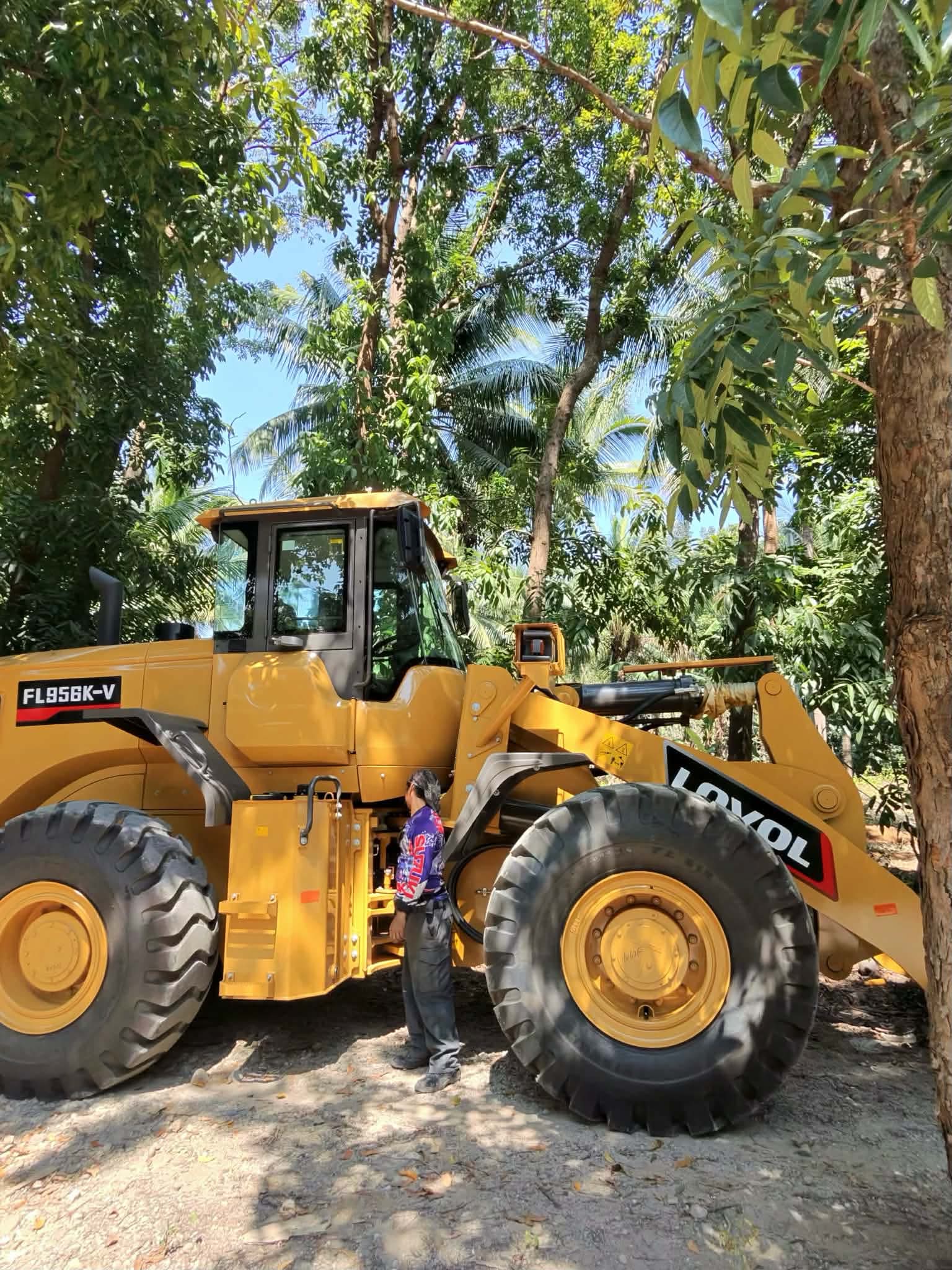Side profile of a large HBR wheel loader in a tree-lined area